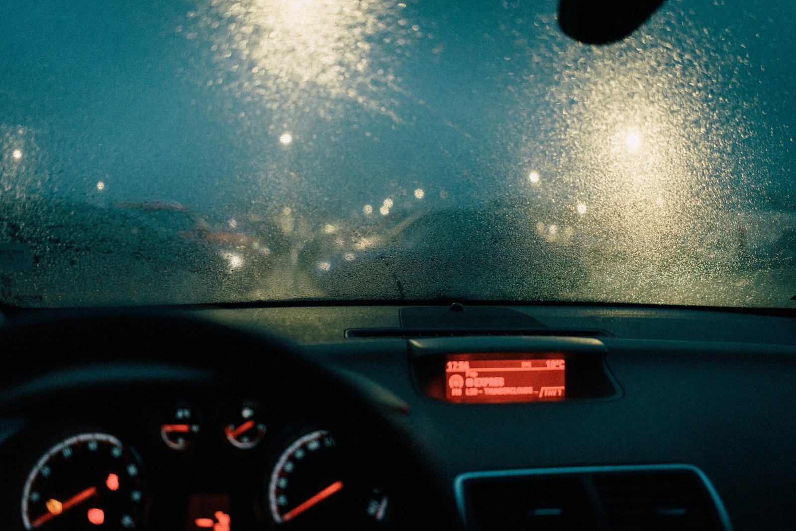 Home View from car interior with raindrops on windshield and blurred lights at night.