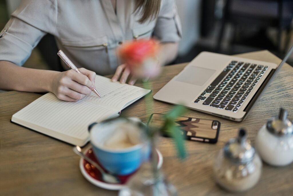 our services Woman writing in a notebook with a laptop and coffee cup on a desk. Ideal for workspace inspiration.