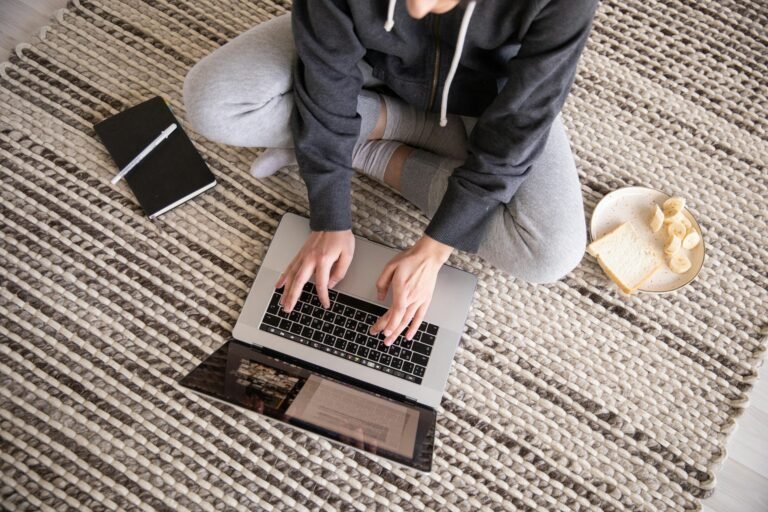 Email Marketing Woman in casual wear working remotely on a laptop, with a notebook and snack nearby.