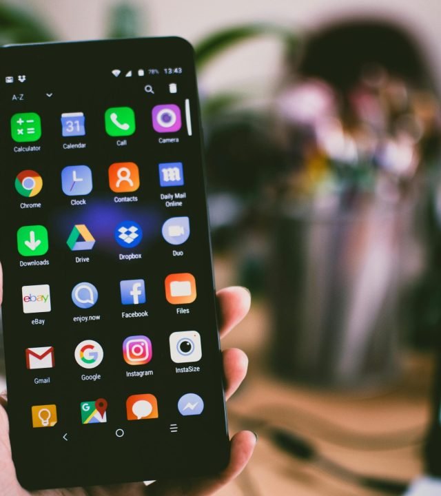 A close-up image of a person's hand holding a smartphone displaying various popular apps.