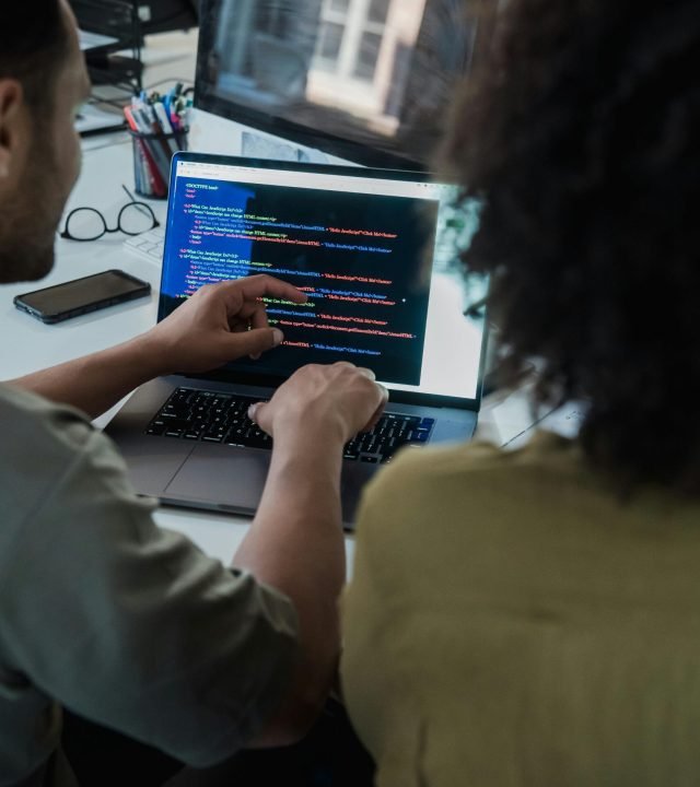 Two adults collaborating on programming tasks using a laptop in an office setting.