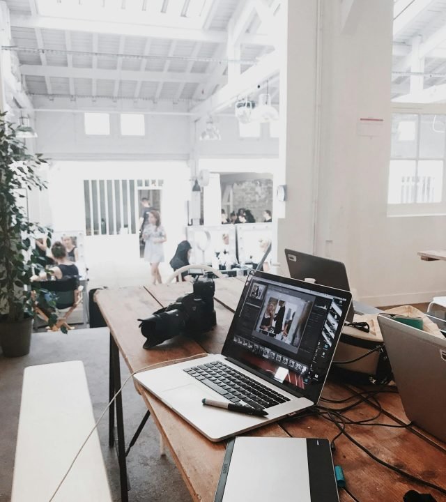A bright, modern workspace featuring laptops, a camera, and a drawing tablet in an indoor office.
